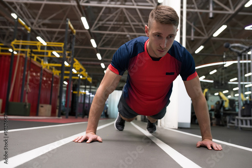 Full length Portrait of handsome young man doing fitness exercises on floor in modern gym warming up before work out, copy space