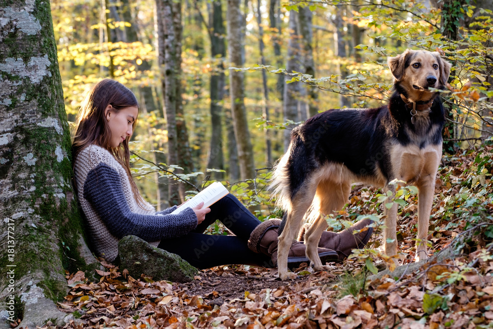 happy young girl reading a book with her dog in autumn forest