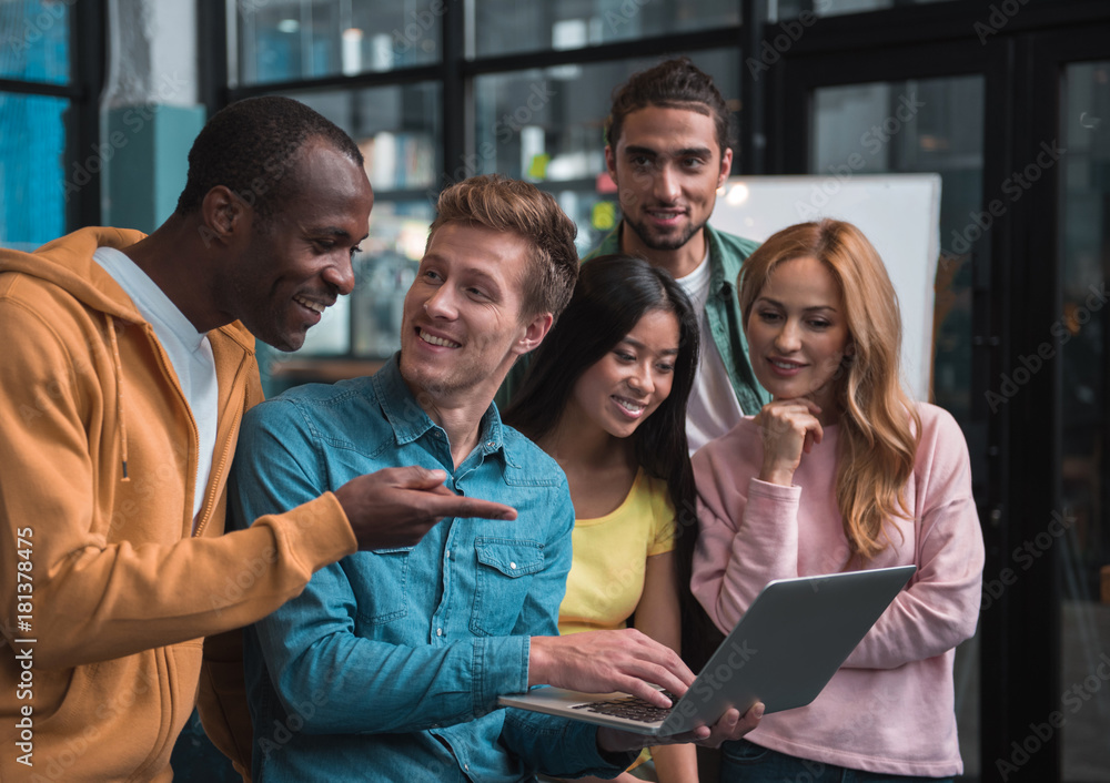 Look here. Optimistic qualified young multinational team is expressing gladness while looking at screen of laptop and working together. African man is pointing on monitor and smiling Look here. Optimistic qualified young multinational team is expressing gladness while looking at screen of laptop and working together. African man is pointing on monitor and smiling
