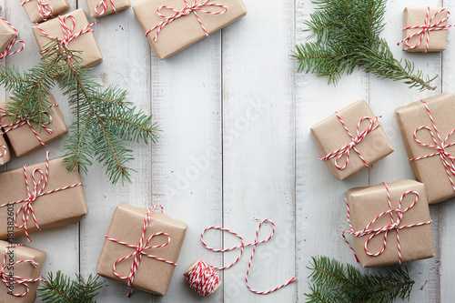 Christmas presents and gift boxes wrapped in kraft paper and fir tree decorations on white wooden background, copy space