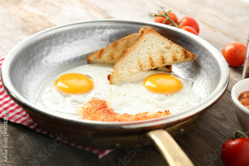 Frying pan with eggs, toasts and bacon on table