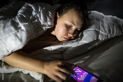 Pretty young brunette woman playing with mobile during night, pending / nighters in bed photo