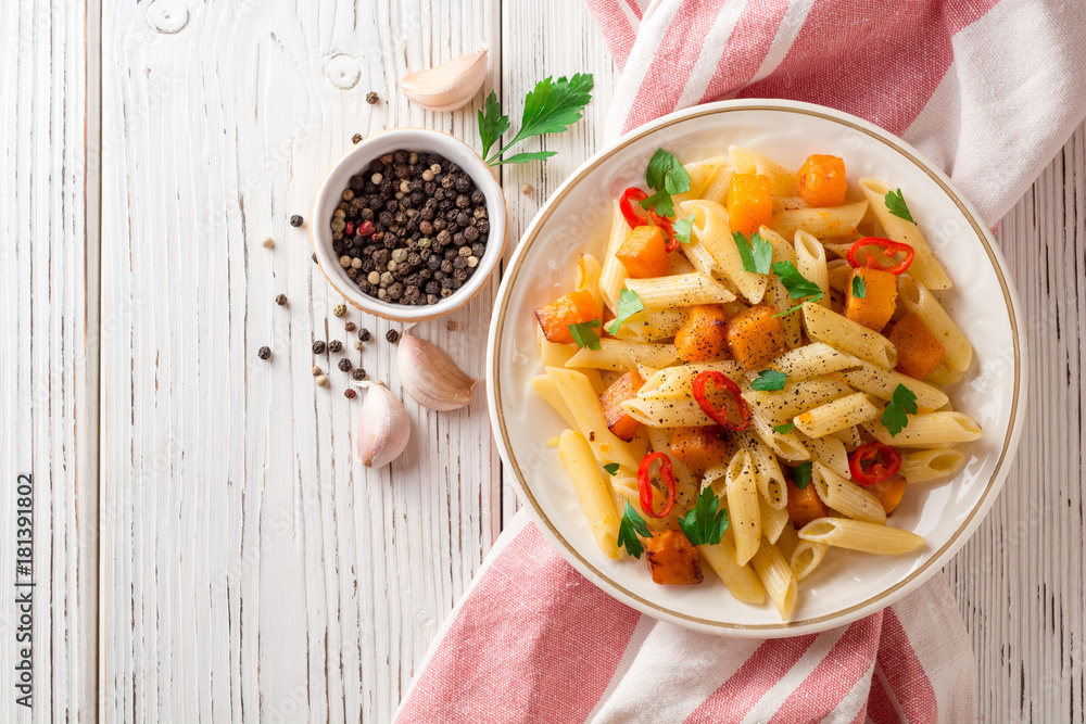Penne pasta with pumpkin, chilli and parsley in plate on white wooden background Penne pasta with pumpkin, chilli and parsley in plate on white wooden background