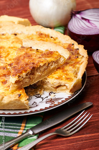 Appetizing French onion pie in a cut. Portion of vegetable vegetarian pie with cheese crust. The table is served for dinner. Simple rustic homemade food.