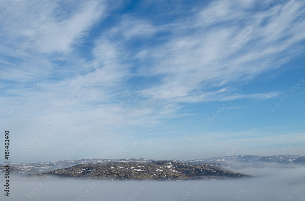 The hills are covered with fog and blue sky with clouds.