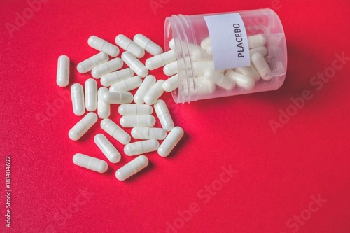 White placebo pills or capsules spilling out of bottle or white plastic container on colorful background, placebo treatment or effect concept