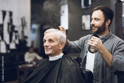 The hairdresser does a hairstyle to an old man with gray hair in a barbershop.