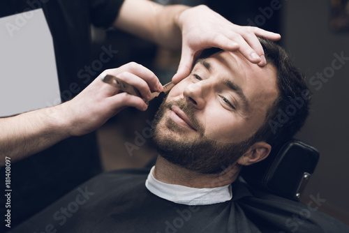 The barber shaves his head, mustache and beard to the man in the barbershop.