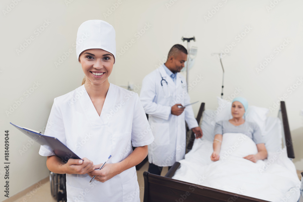 A nurse is posing against the patient's background. She holds a paper tablet in her hands.