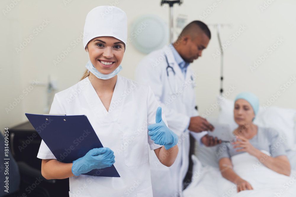 A nurse is posing against the patient's background. She holds a paper tablet in her hands. A nurse is posing against the patient's background. She holds a paper tablet in her hands.