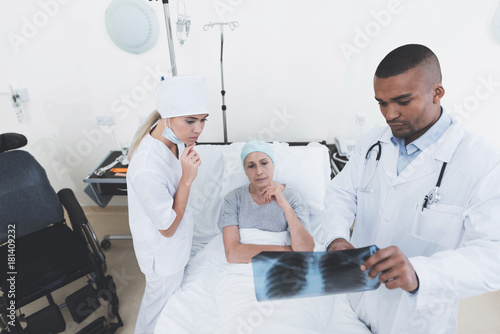 A nurse and a doctor are standing next to a patient with cancer. The doctor is holding her X-ray.