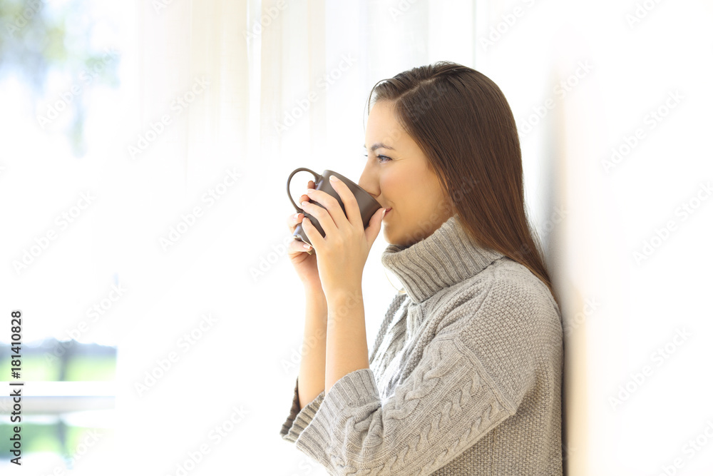 Woman drinking coffee looking through a window Woman drinking coffee looking through a window