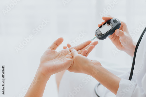 Doctor use glucosmeter checking blood sugar level from patient hand photo