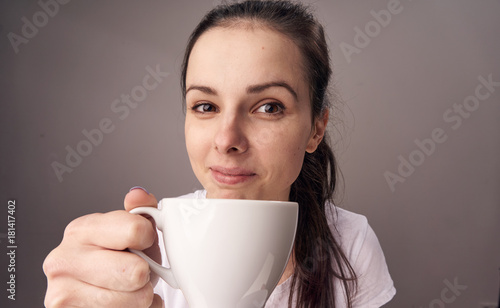 Young woman on a gray background holds a mug
