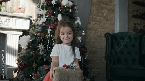 Little beautiful girl standing near a Christmas tree and holding a Christmas gift in the box photo