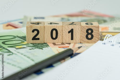 financial tax concept as number 2018 on wooden cube block on pile of euro banknotes with note paper and pencil