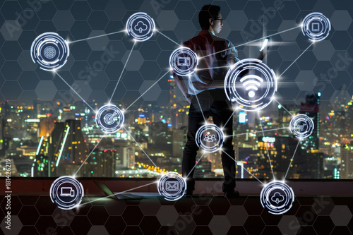 Asian businessman standing and using the smart mobile showing Wireless communication connecting of smart city Internet of Things Technology over cityscape background,technology business IOT concept