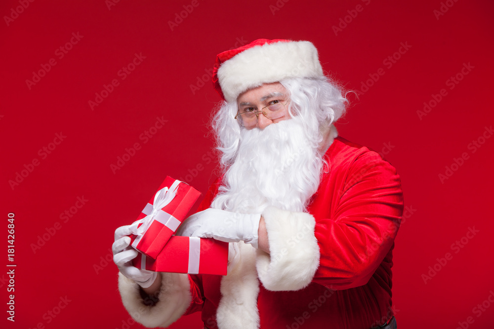 Naklejka premium Christmas. Photo Santa Claus giving xmas present and looking at camera, on a red background