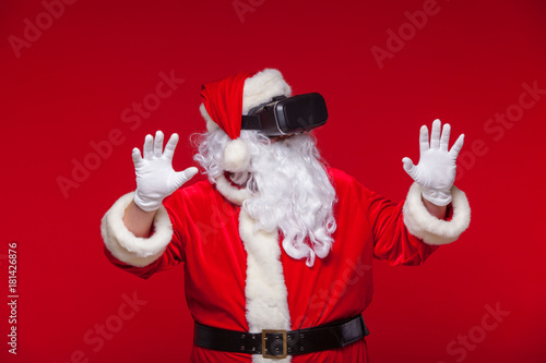 Santa Claus wearing virtual reality goggles, on a red background. Christmas photo