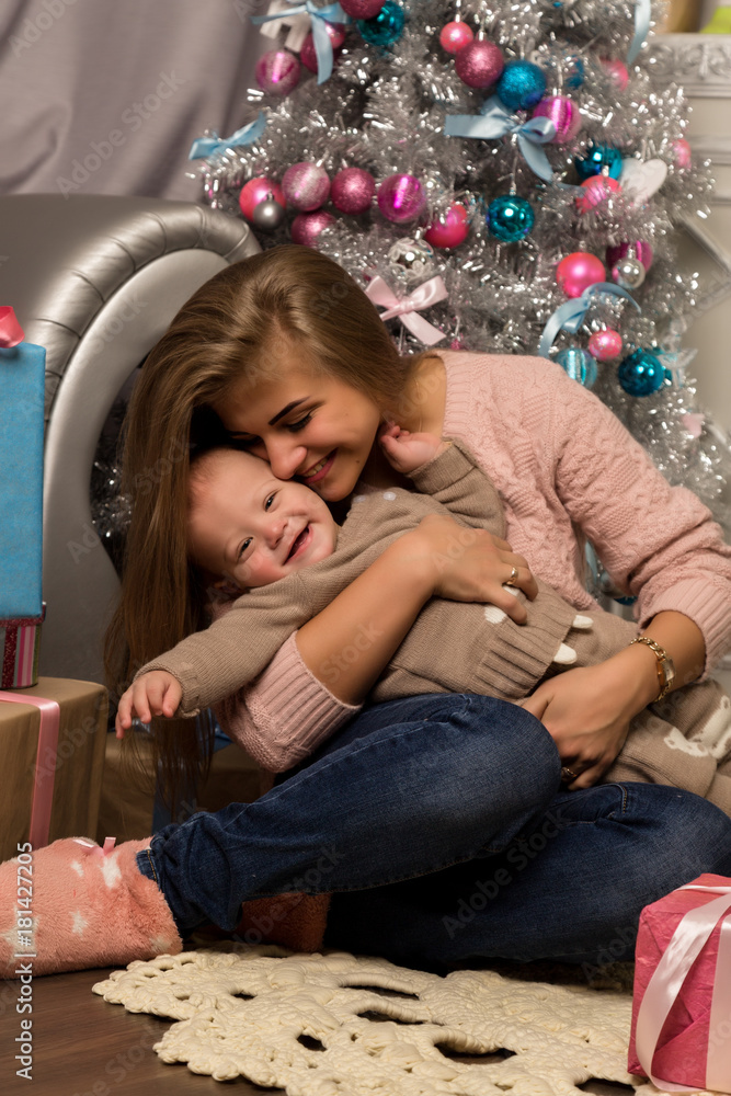 Happy mother with newborn son, sitting on a floor near a Christmas tree. Waiting for a holiday. Happy mother with newborn son, sitting on a floor near a Christmas tree. Waiting for a holiday.