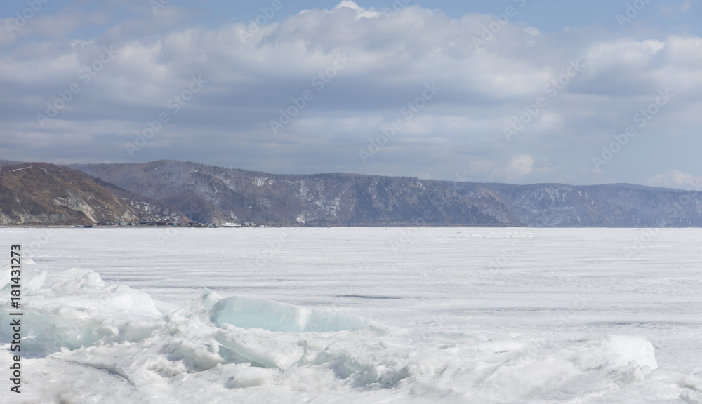 Transparent blue ice hummocks on lake Baikal shore. Siberia winter landscape view. Snow-covered ice of the lake. Big cracks in the ice floe.