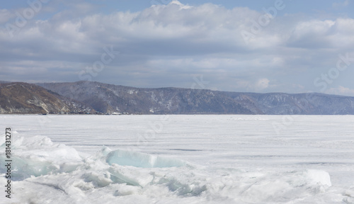 Transparent blue ice hummocks on lake Baikal shore. Siberia winter landscape view. Snow-covered ice of the lake. Big cracks in the ice floe.