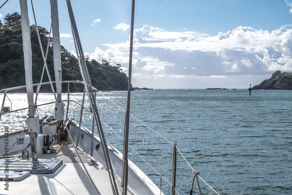 Obraz premium Sailboat yacht motoring out of Tutukaka Harbour between rocks and navigational channel marker in Northland, New Zealand, NZ