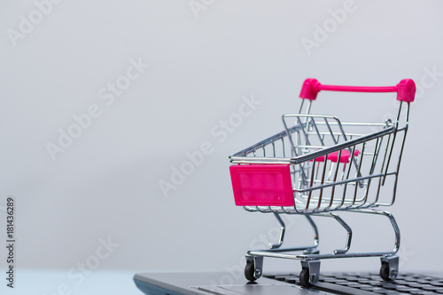 Shopping cart or supermarket trolley with laptop notebook isolated on grey background, e-commerce and online shopping concept.