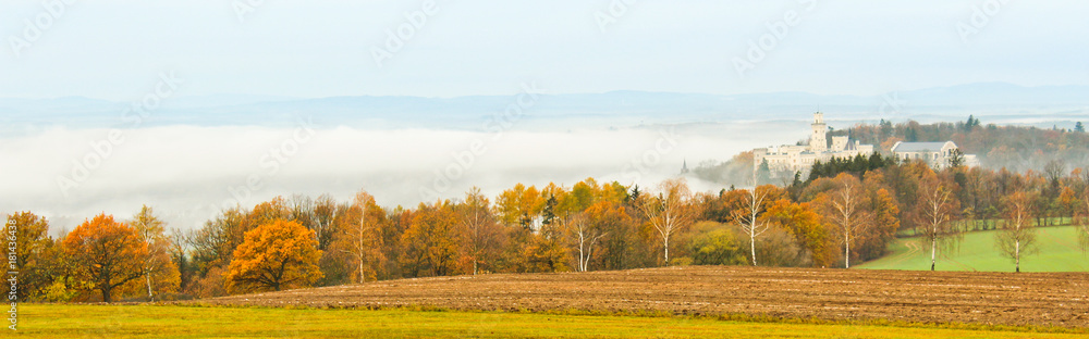 Castle Hluboka nad Vltavou with autumn trees and fog, Czech landscape