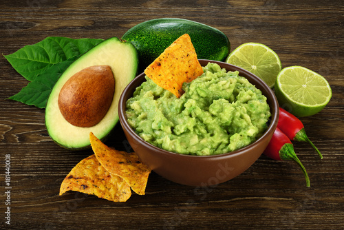 Guacamole nachos and guacamole ingredients on dark wooden background.