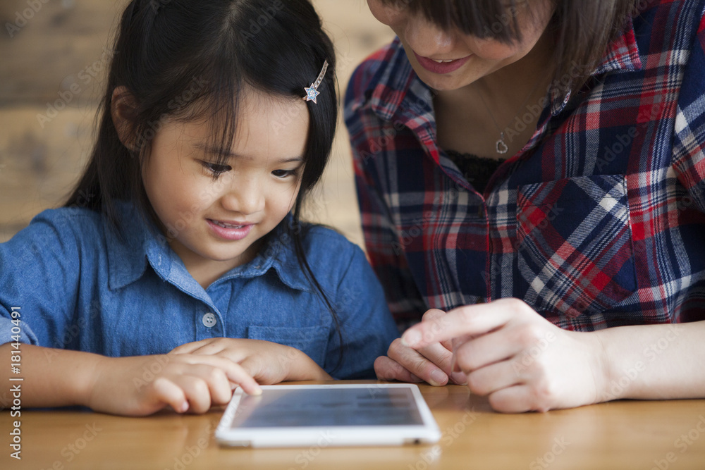 Mother and daughter are using a digital tablet at the table together. Mother and daughter are using a digital tablet at the table together.