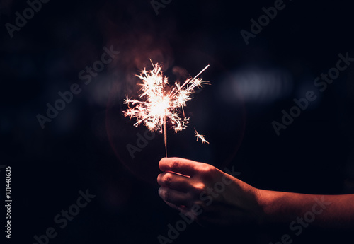 Hand holding burning Sparkler blast on a black background at night,holiday celebration event party,dark vintage tone. photo