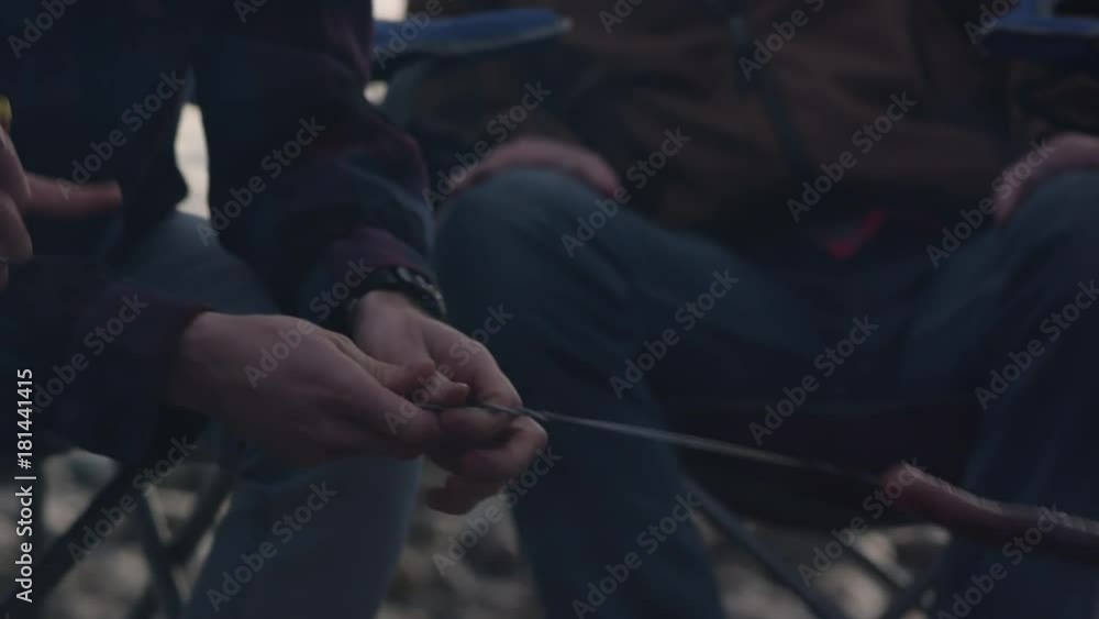 Hot dog roasting over campfire then pannng up to young men talking in group on cold evening. Hot dog roasting over campfire then pannng up to young men talking in group on cold evening.