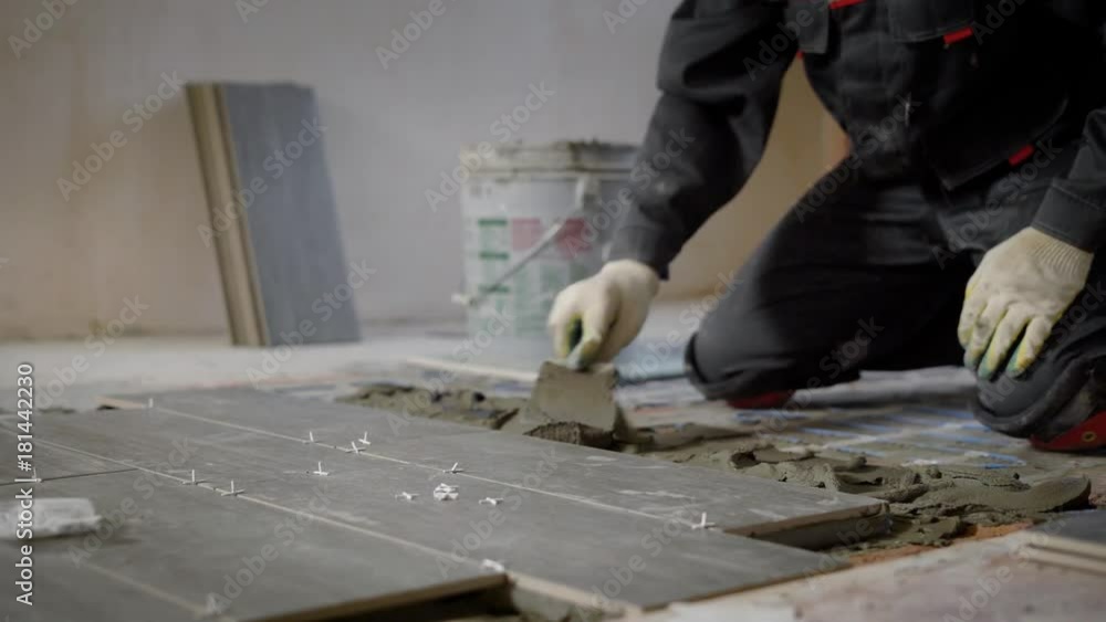 tiler is applying a building mixture on a floor for montage of ceramic tiles, master is standing on a knees on a floor tiler is applying a building mixture on a floor for montage of ceramic tiles, master is standing on a knees on a floor