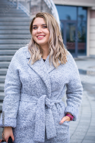 A woman of plus size, American or European appearance walks in the city enjoying life. A young lady with excess weight, stylishly dressed in coat at the center of the city. Natural beauty