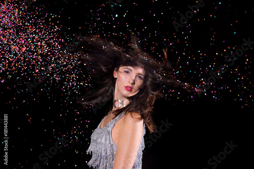 A young girl stands in front of a black background and is surrounded by confetti explosions. She laughs and smiles in her role as the party girl.