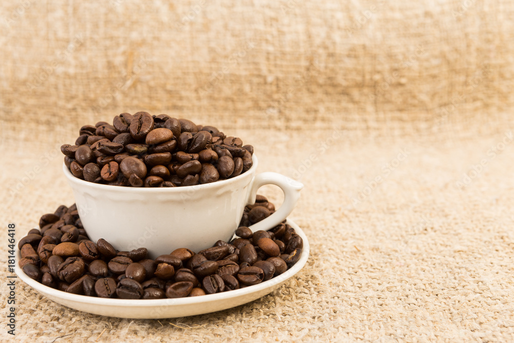 Fototapeta premium Coffee cup filled with roasted beans on jute text area