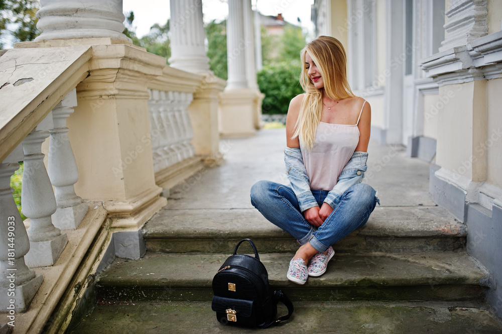 Blonde girl wear on jeans with backpack posed against vintage house. Blonde girl wear on jeans with backpack posed against vintage house.