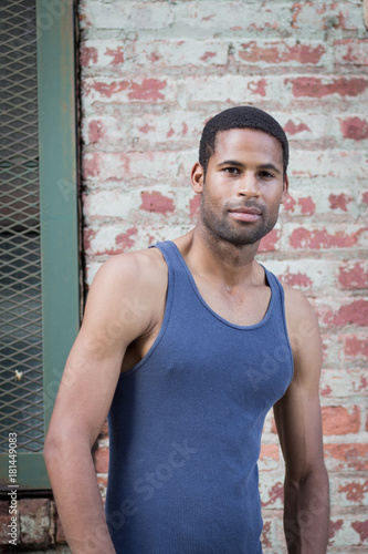 Portrait of young handsome African American man in tank top against brick wall