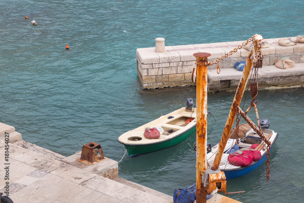 Two boats near stone pier and  rusty hoist