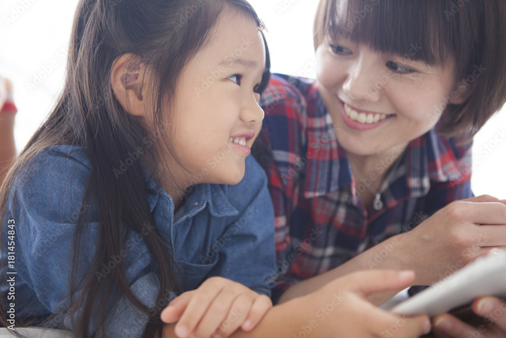 Mother and daughter are using a digital tablet at the table together. Mother and daughter are using a digital tablet at the table together.
