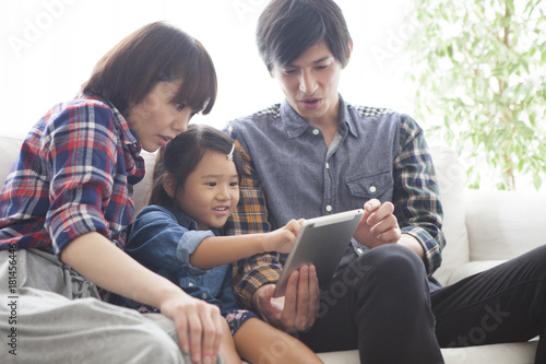 Parents and daughter are sitting on the sofa and using a digital tablet together.