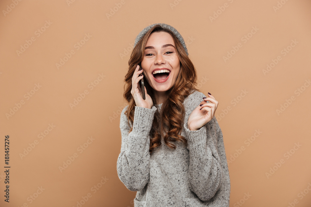 Fototapeta premium Portrait of beautiful laughing brunette woman in warm clothes talking on mobile phone, looking at camera
