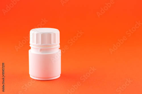 Close up white pill bottle on orange background with copy space. Focus on foreground, soft bokeh. Pharmacy drugstore concept
