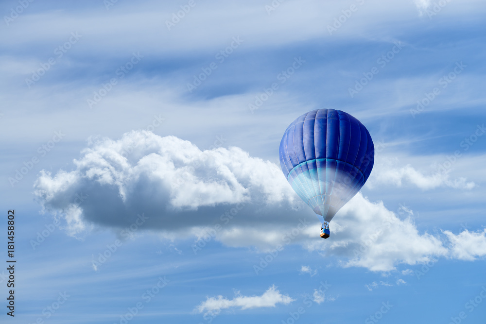 Obraz premium Hot air blue ballon against blue sky with white fluffy clouds and copyspace for text
