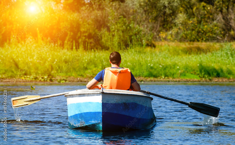 Man in life jacket rowing a boat over clear water on the river in