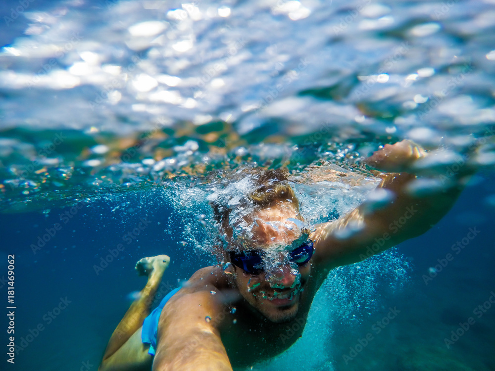 Underwater view of a young playful happy man relaxing and enjoying at the sea for summer holidays while taking a selfie.