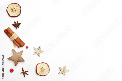 Christmas festive styled stock image composition. Decorative pattern. Cinnamon sticks, red berries, dried apple fruit, anise and wooden stars isolated on white wooden background. Flat lay, top view.
