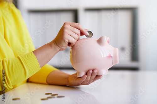 Close up of woman putting coin into piggy bank