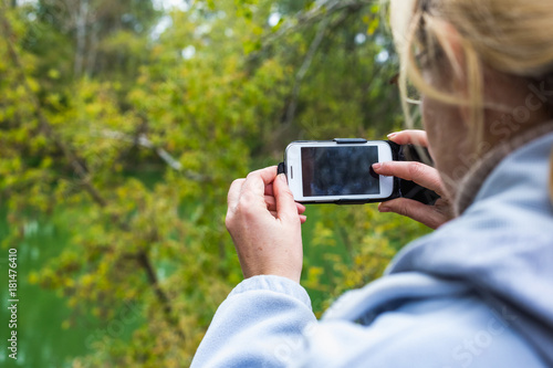 A blonde woman using a phone takes a photo of a beautiful landscape